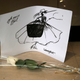 A flower and a drawing are displayed by well-wishers at Chanel's headquarters in Paris in tribute to fashion designer Karl Lagerfeld France, Tuesday, Feb. 19, 2019. Chanel's iconic couturier, Karl Lagerfeld, whose accomplished designs as well as trademark white ponytail, high starched collars and dark enigmatic glasses dominated high fashion for the past 50 years, has died. He was around 85 years old. (AP Photo/Michel Euler)